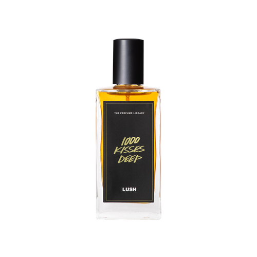 A glass perfume bottle filled with amber liquid. A black label reads 'The Perfume Library' and '1000 Kisses Deep'.