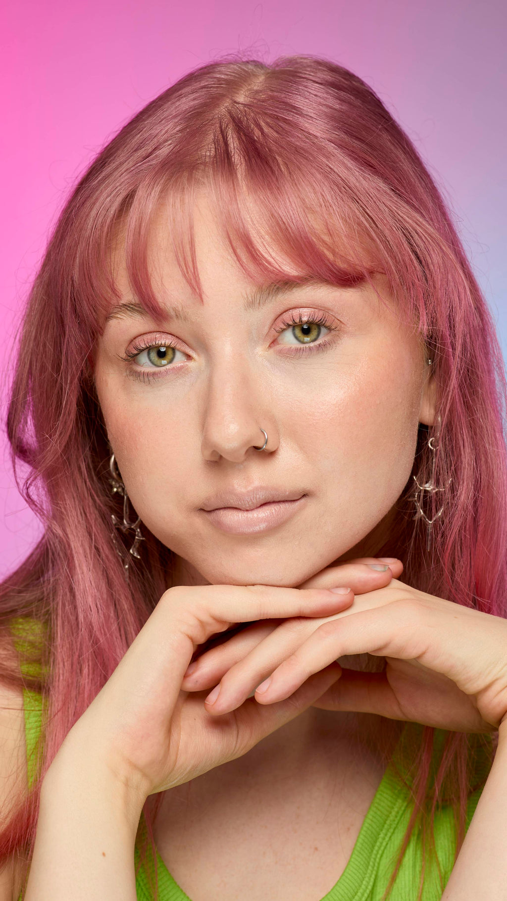 The image shows a fair-skinned model on a pink and blue gradient background. They have pink hair and subtle, peach-nude shimmering lips from using the Peach parfait lip cream.