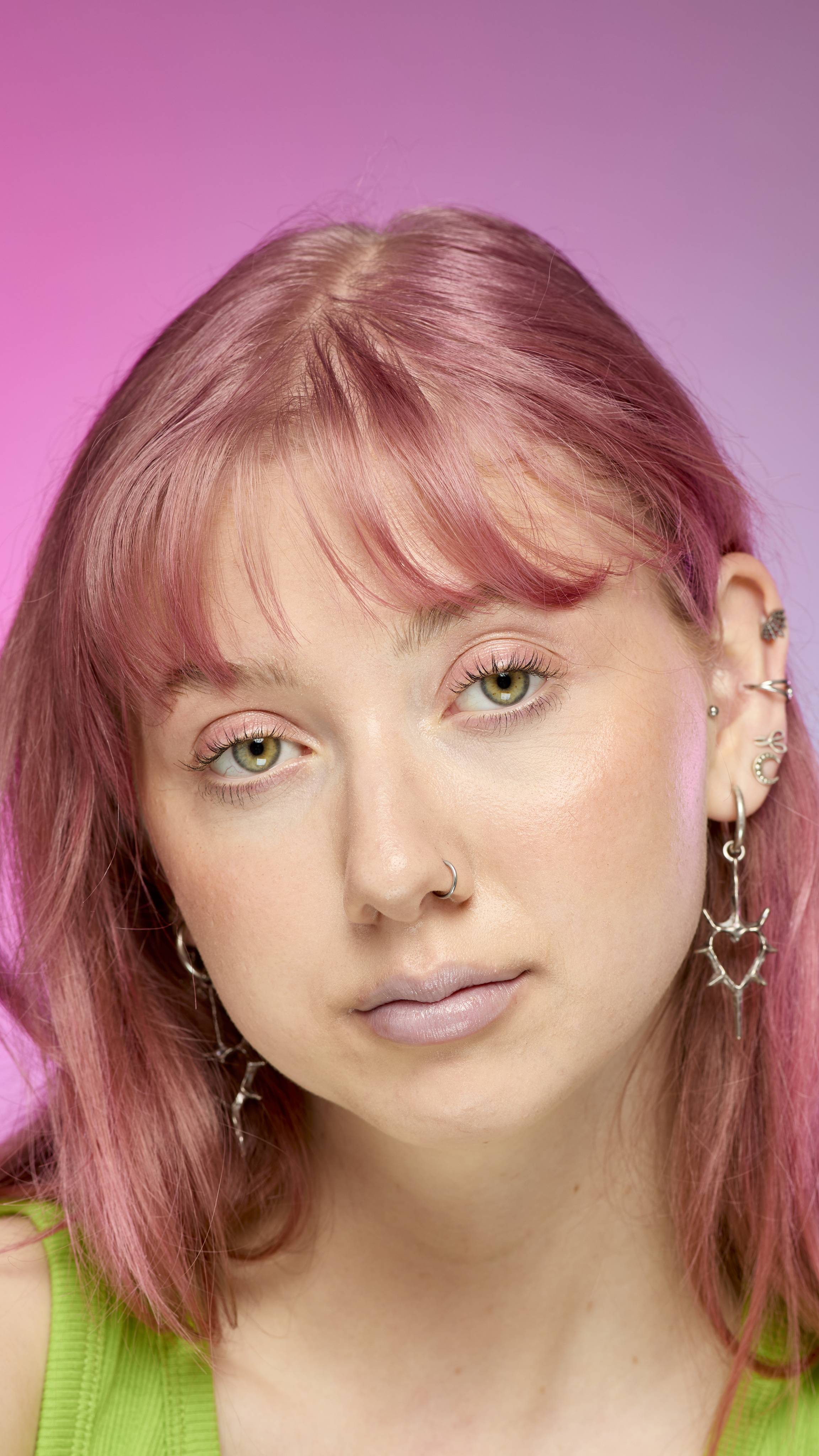 The image shows a fair-skinned model on a pink and blue gradient background. They have pink hair and subtle, blue shimmering lips from using the Blue Pearl lip cream.