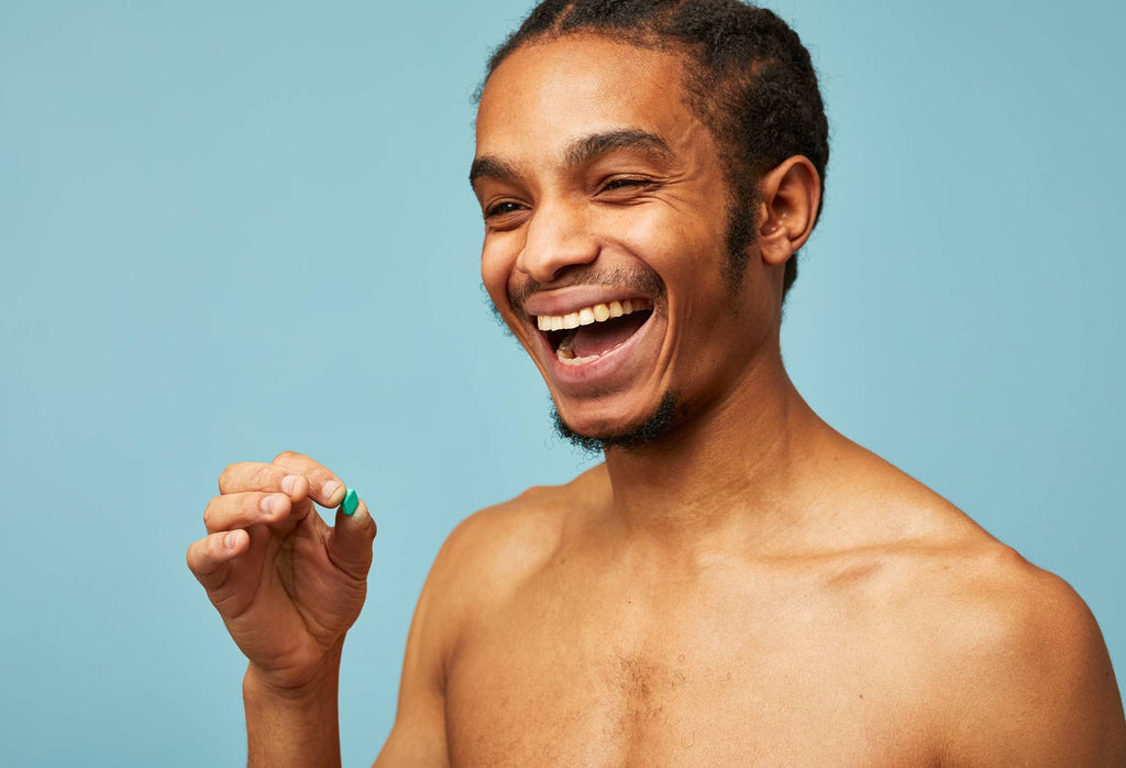 A person prepares to put a small green mouthwash tab into their open mouth with their hand.