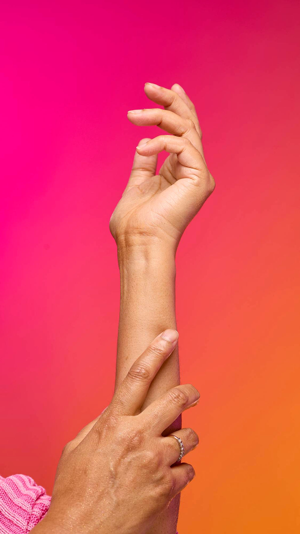 The image shows a model's forearm extended from the bottom as the skin appears moisturised with a subtle, delicate shimmer over the skin after having used the Golden Egg Glitter Mist spray product on a pink-to-orange gradient background.