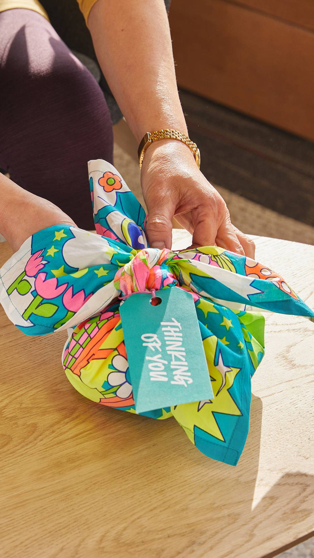 The image shows the model attaching the written gift tag to the neatly wrapped Joyous Springtime knot wrap and gift.