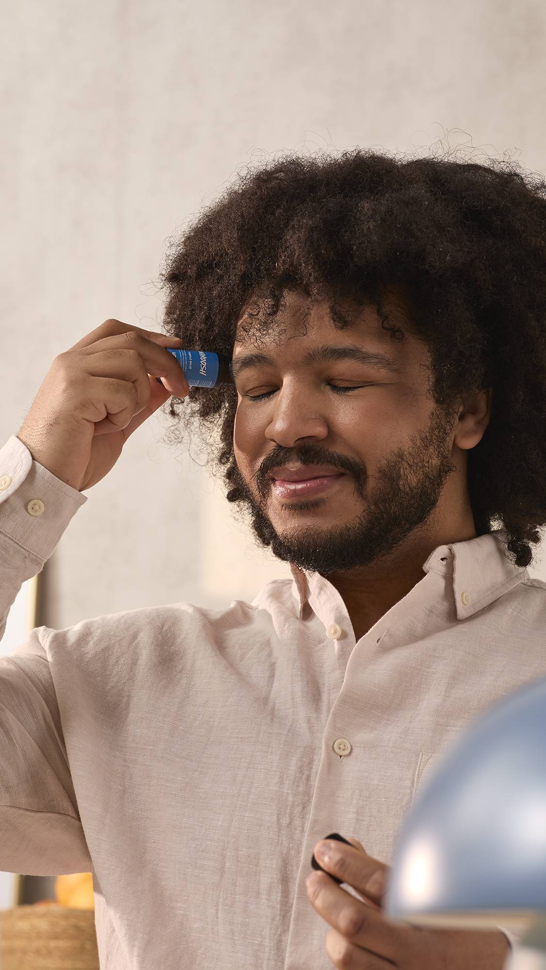 The model is in a naturally bright room in a pale shirt. They are gently applying the Whoosh balm directly to their temple as their eyes are closed in satisfaction.